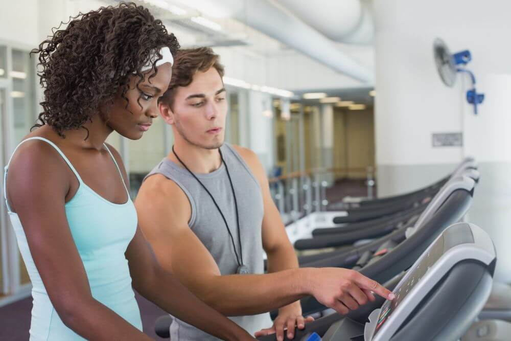 A black woman getting treadmill maintenance tips from her instructor